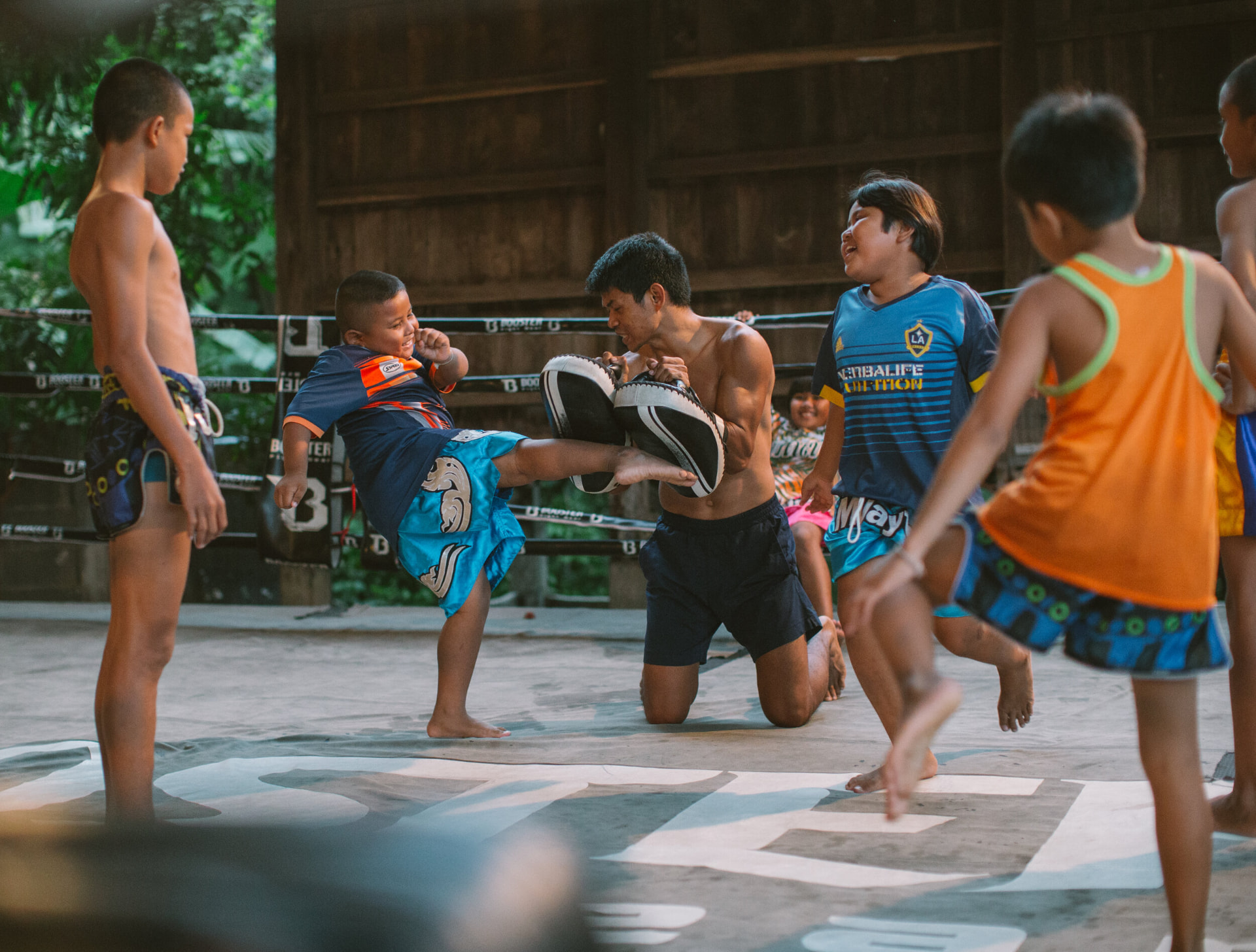 A coach holding pads for a smiling young student in the ring while other children wait their turn.
