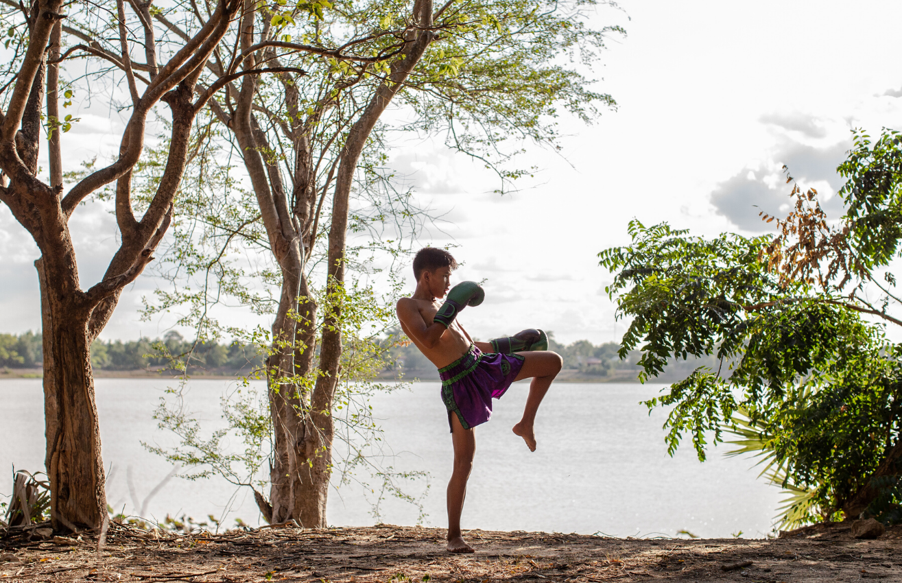 A young Wor. Watthana student practising a kick beside the river at sunrise in Isaan, Thailand.