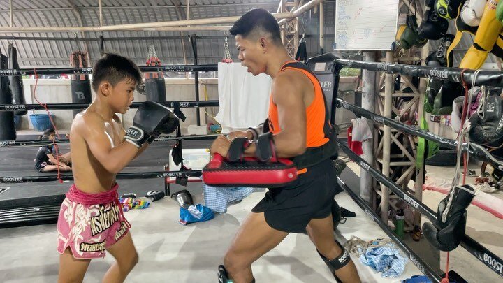A young student throwing punches on the pads with his coach inside the ring at Wor. Watthana.