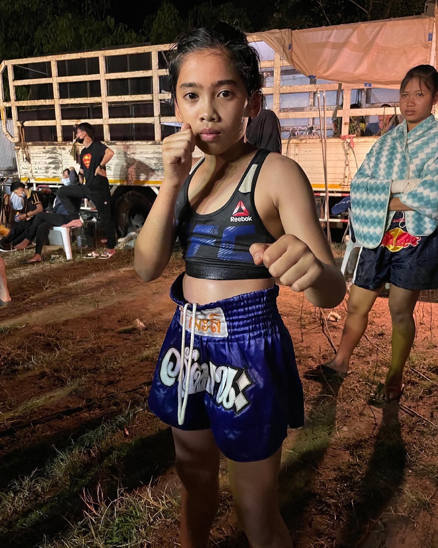 A young fighter in blue Muay Thai shorts holding her guard before a local fight night.